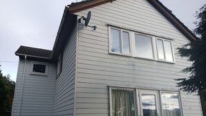 Une maison à deux étages, avec un revêtement extérieur blanc, une antenne parabolique et une porte de garage.