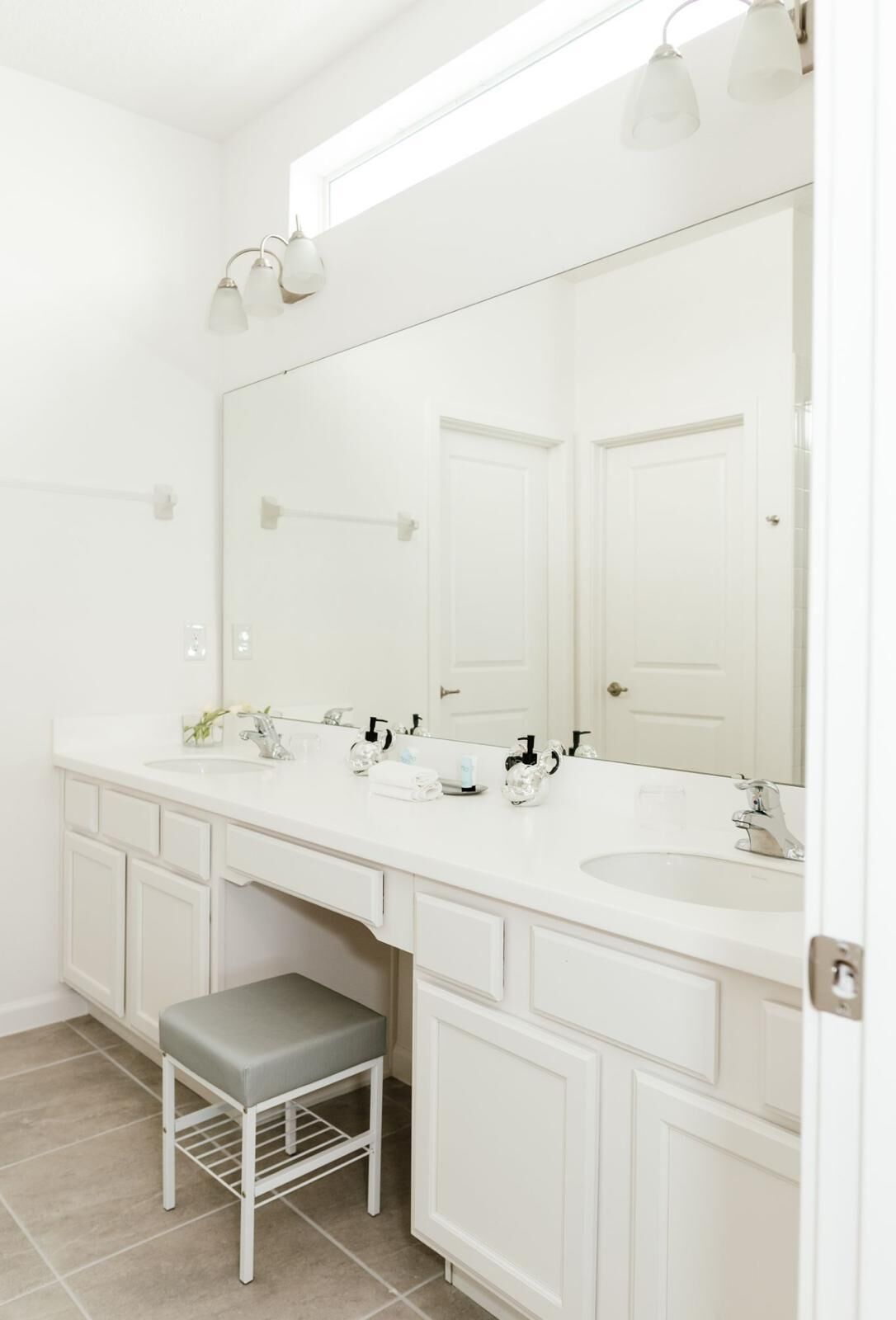 A bathroom with a double sink vanity, a large mirror, and a stool.