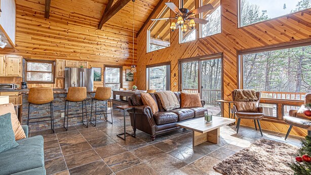Eine geräumige Holzhütte mit hohen Decken, rustikalem Interieur, einem Steinofen und großen Fenstern mit Blick auf den umliegenden Wald.
