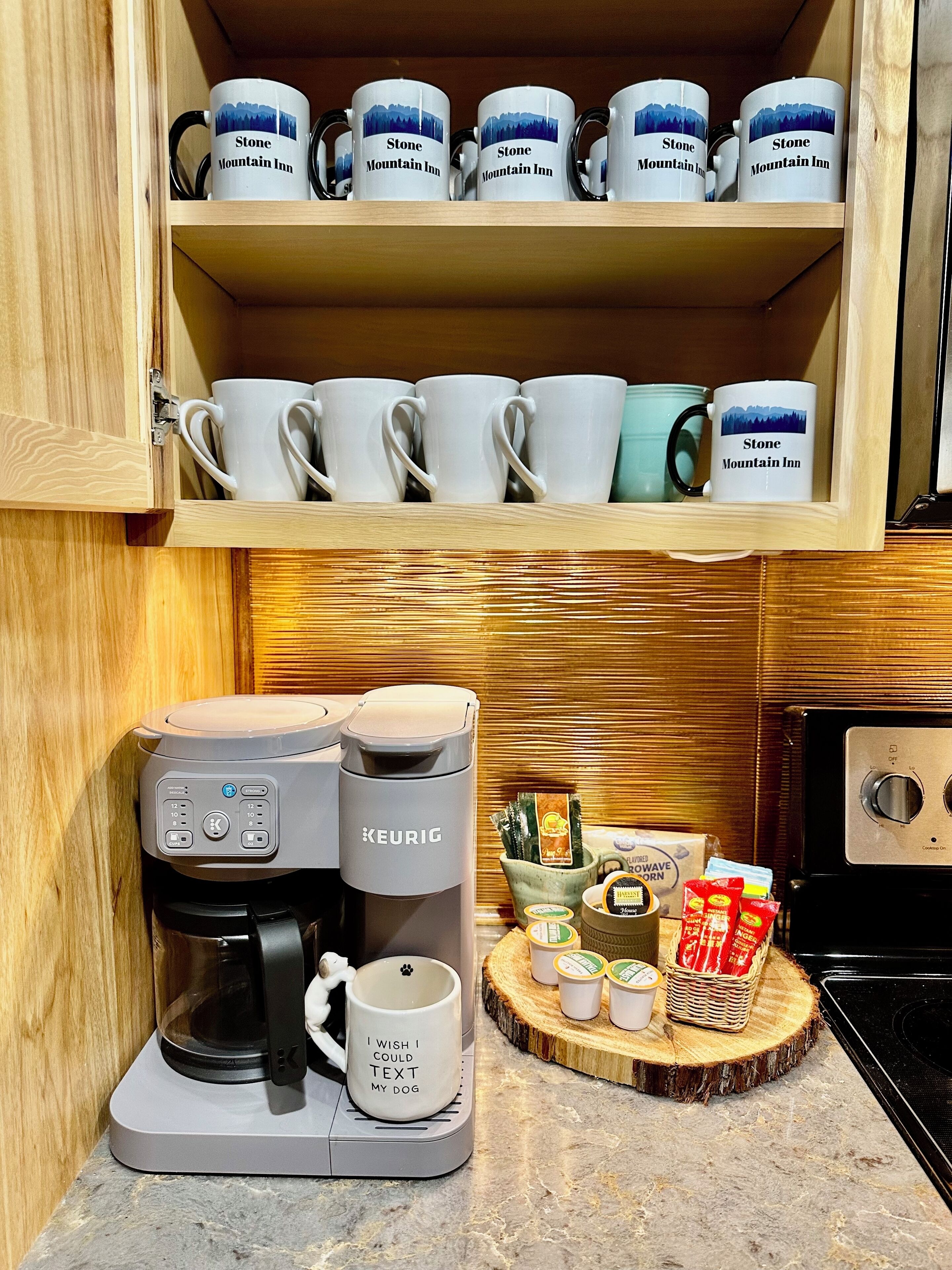 A kitchen with a coffee maker, a mug with a dog text, and a shelf with multiple mugs.