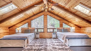 Ein gemütliches Schlafzimmer im Dachgeschoss mit zwei Betten, einem großen Fenster und einem Deckenventilator.