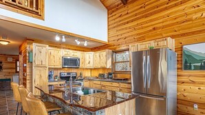 Eine moderne Küche mit Holzschränken, einem Edelstahlkühlschrank und einer Stein-Kochinsel mit Barhocker.