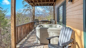 Eine Holzterrasse mit Whirlpool, Stuhl und Tisch, mit Blick auf eine Berglandschaft.