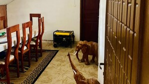 Uma escadaria com corrimãos de madeira, uma área de refeições com cadeiras e mesa de madeira, e uma pequena estátua de elefante no chão.