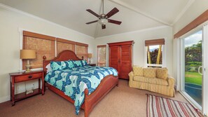 A bedroom with a bed, a nightstand, a wooden wardrobe, a chair, a ceiling fan, and a window with a view of greenery. - Privacy and Elegance in Princeville (Princeville)