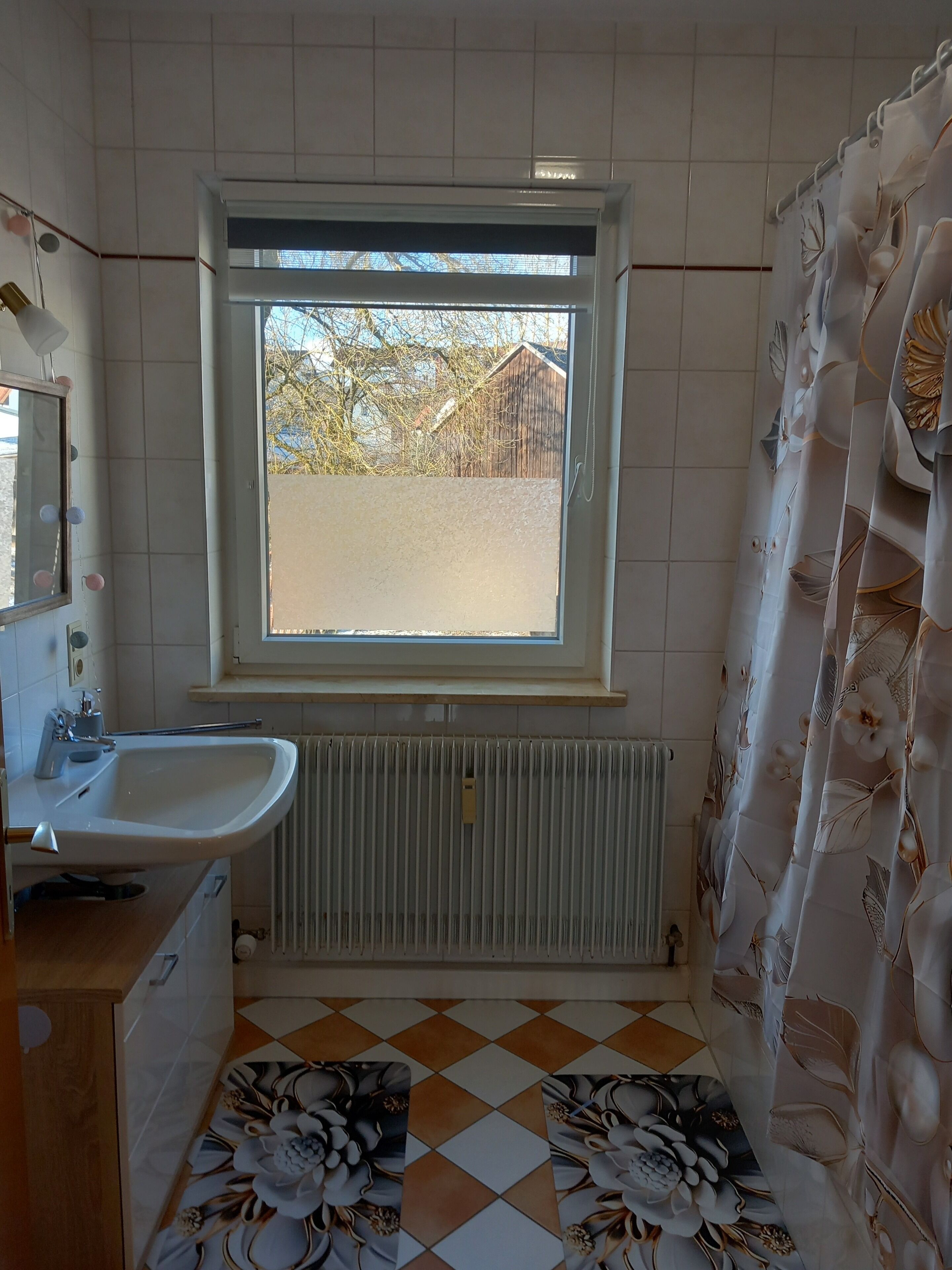 Un baño con ventana, lavamanos, radiador y baldosas de suelo estampadas.