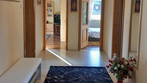 A hallway with a bench, a large dark patterned rug, and a potted plant with red and white flowers. - Sylvia's castle view (Trausnitz)