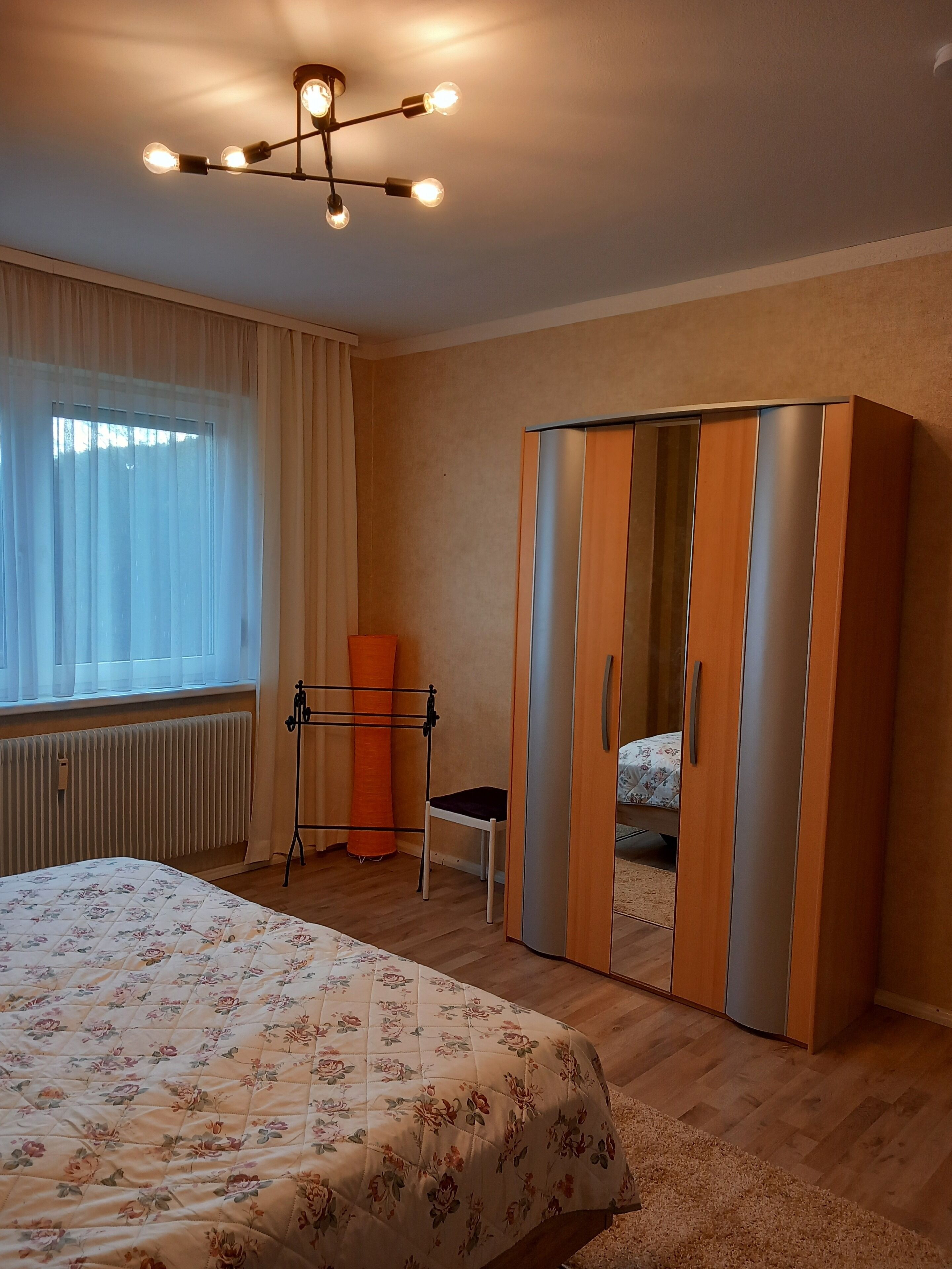 Un dormitorio con cama, armario, radiador y ventana con cortinas.