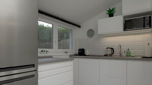 Una cocina moderna con armarios blancos, un refrigerador de acero inoxidable, un microondas y una ventana con plantas en el alféizar.