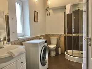 Een moderne badkamer met een wasmachine, toilet en douchecabine.