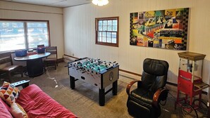 Ein Zimmer mit Kicker, einer Couch, einem Sessel, einem Tisch mit Stühlen und einem Wandbild.