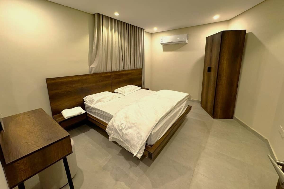Een slaapkamer met een houten bed, een nachtkastje, een airconditioning en een kledingkast.