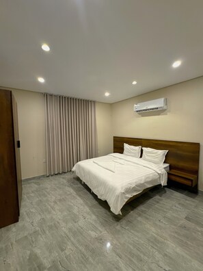 Habitación de hotel moderna con una cama grande, cabecera de madera, aire acondicionado instalado en el techo y un ventanal con cortinas.