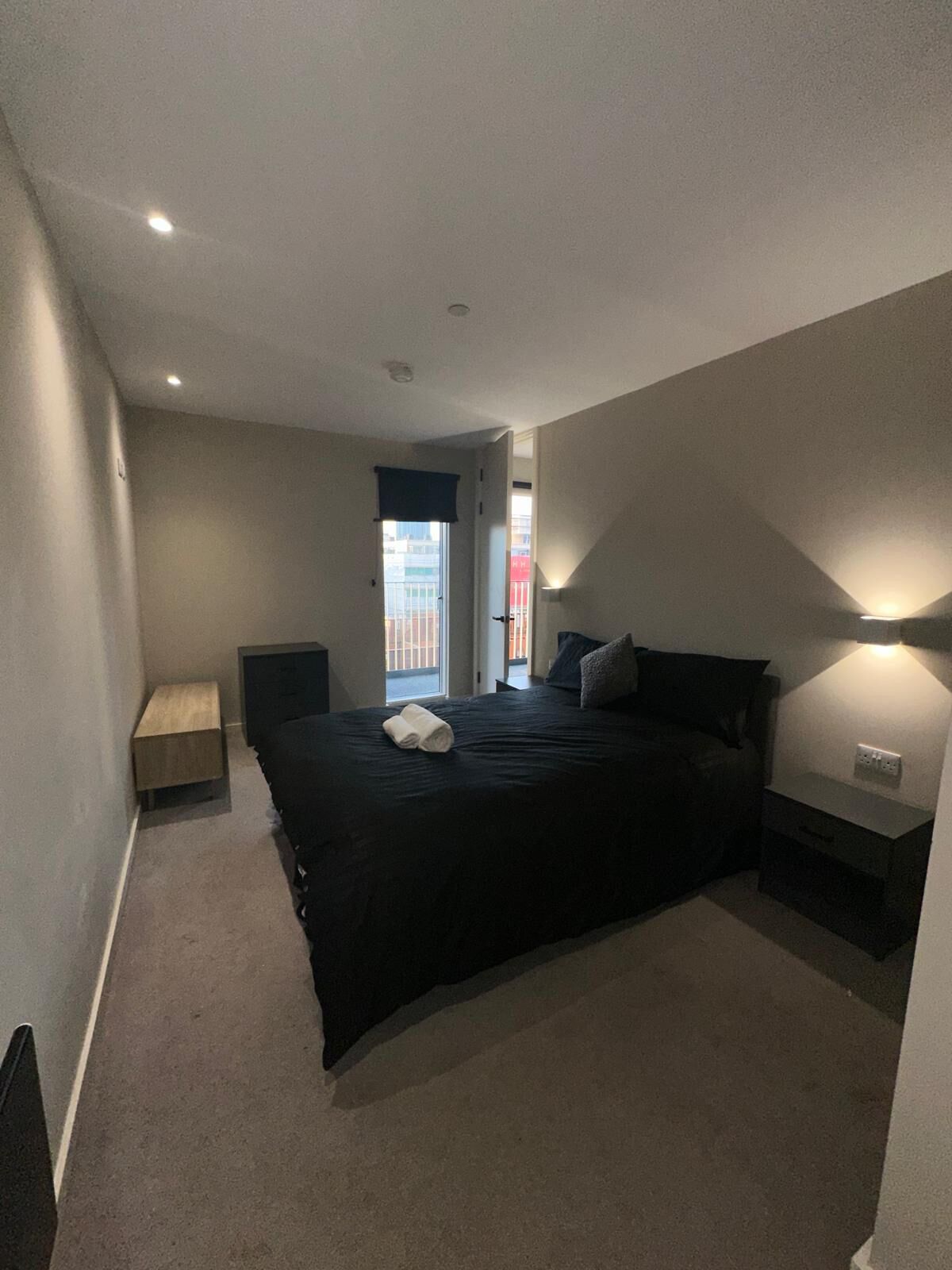 A bedroom with a bed, bedside tables, a nightstand, a window with a view, and a door leading to another room.