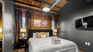 A modern bedroom with a large bed, a wooden ceiling, and a brick wall.