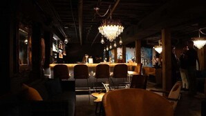 A dimly lit bar area with a bar counter, multiple chairs, and a chandelier.