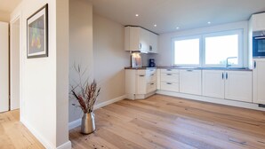Una cucina moderna con mobili bianchi, pavimento in legno e una finestra che lascia entrare luce naturale.