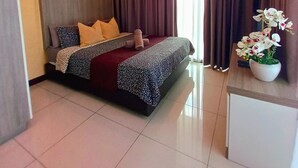 Una habitación de hotel con cama, ventilador de techo, equipo de aire acondicionado, ventana con cortinas y una planta en maceta.