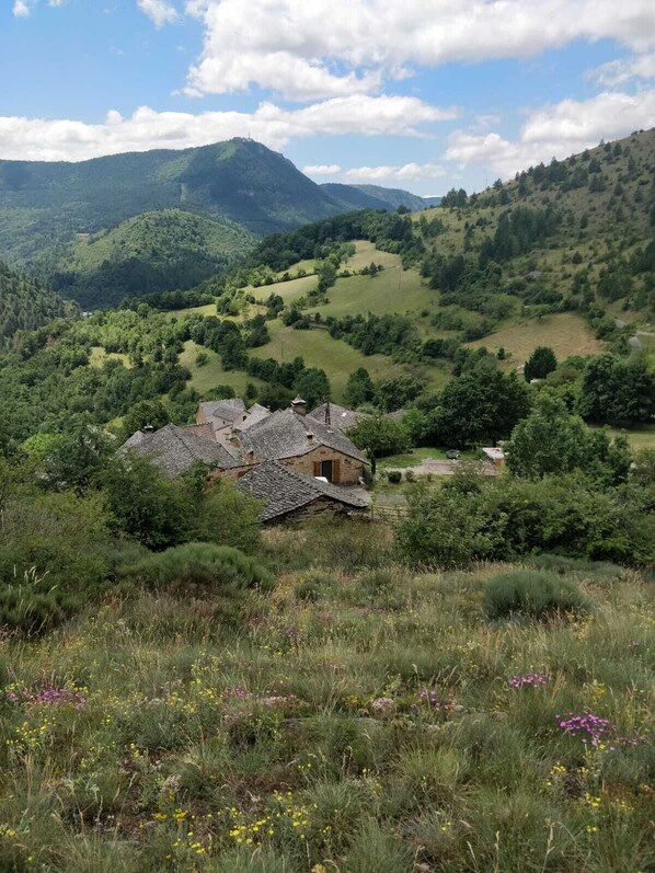 A rural landscape with a stone house surrounded by lush greenery and hills. - Chez Annaïk, a 17th-century farmhouse with an extraordinary view of the Causse Méjean (Ispagnac)