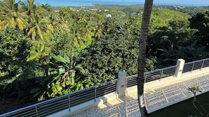 Ein Balkon mit Steinboden, Metallgeländer und Blick auf eine üppige grüne Landschaft und das Meer.