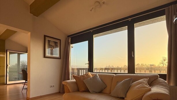 A modern living room with a sofa, a patterned rug, and large windows offering a view.