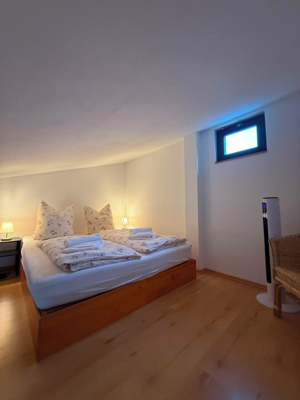 Una camera da letto con un letto, cuscini, un comodino, una lampada e una finestra.
