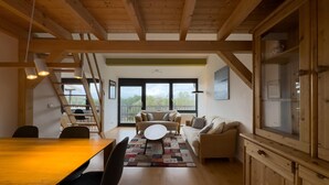 A spacious living area with a wooden ceiling, a dining table, and a sofa set.