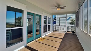 A covered porch with wooden flooring, a ceiling fan, and large windows offering views of the outdoors.