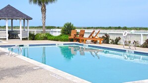 A swimming pool with lounge chairs, a gazebo, and a white fence.