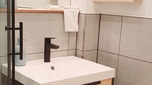 Une salle de bain moderne avec un lavabo blanc, un robinet noir et des étagères en bois pour le rangement.