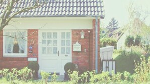 Une petite maison en briques avec une porte blanche, une fen être avec des rideaux et une boîte aux lettres.