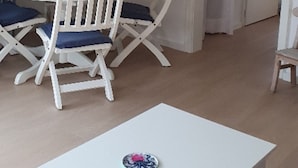 Un coin repas avec une table et des chaises blanches, une affiche accrochée au mur et une porte donnant sur une autre pièce.