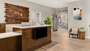 A reception area with a wooden wall, a flat-screen TV, a white counter, and a plant.