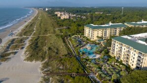 An aerial view of a coastal hotel with a beach, a swimming pool, and multiple buildings.