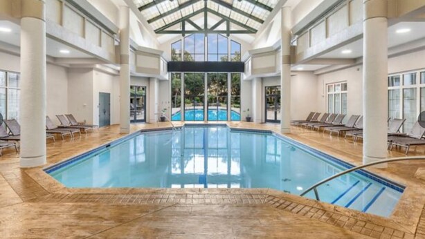 A large indoor swimming pool with clear glass ceilings, multiple lounge chairs, and a view of the outdoors.