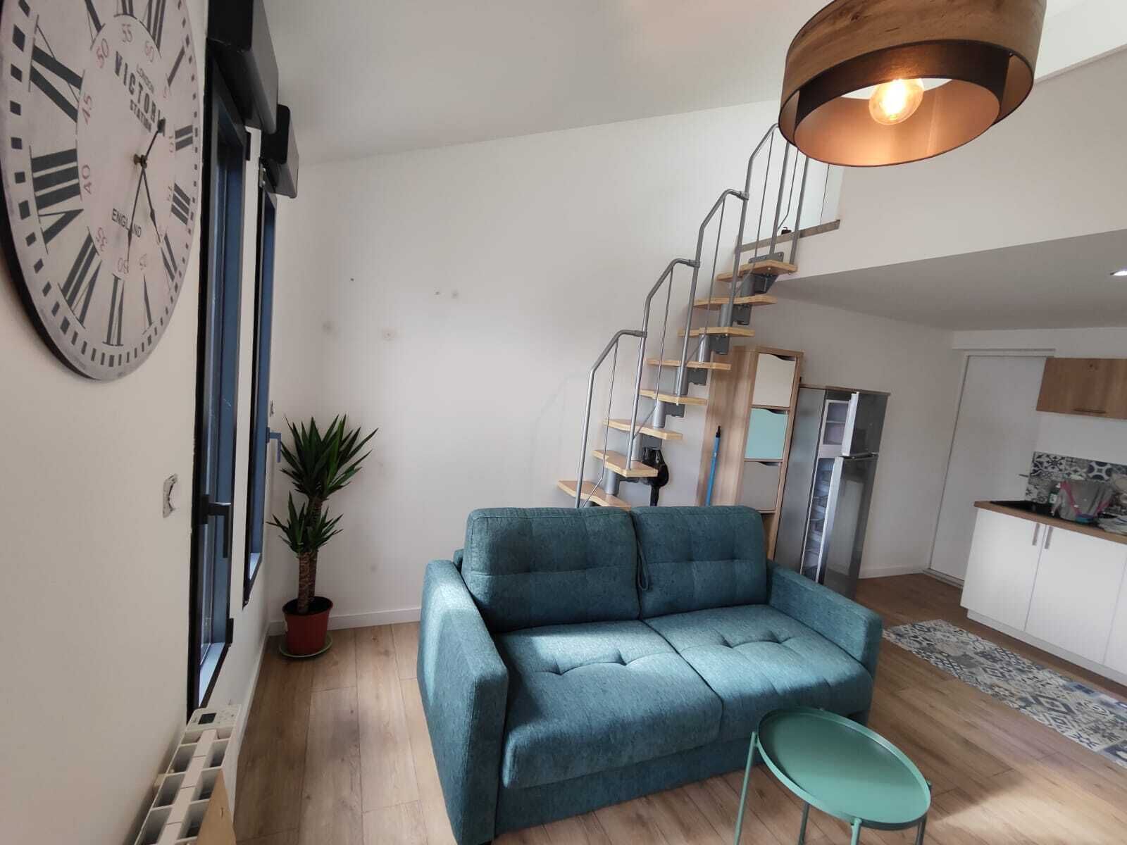 Un salon moderne avec un canapé bleu, une petite table, un escalier et une grande horloge murale.