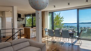 Un salon moderne avec un grand canapé, un coin repas avec des chaises et une vue sur la mer.