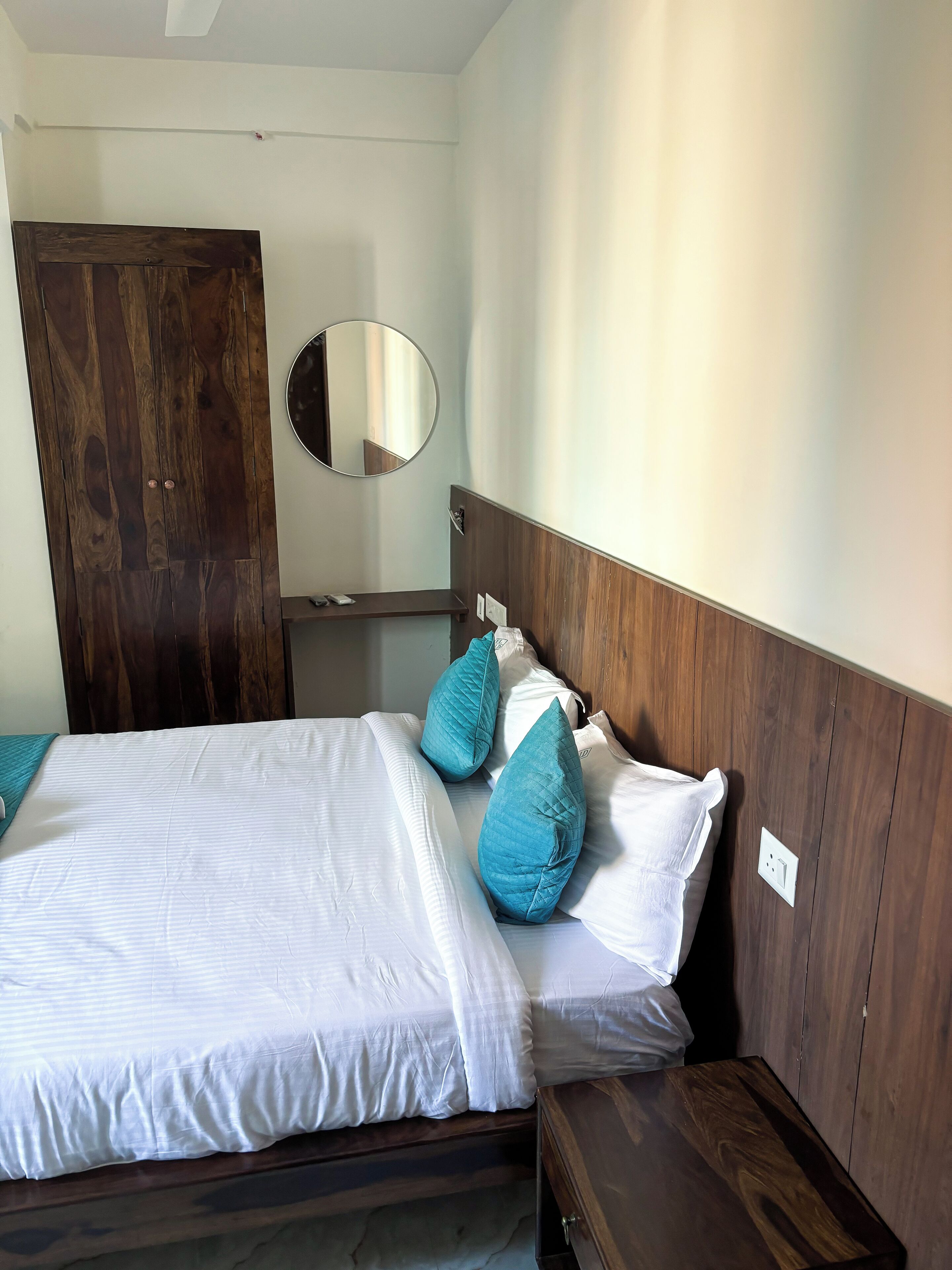 Quarto com duas camas, cabeceiras de madeira, um espelho redondo e um guarda-roupa de madeira.