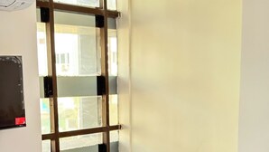 Una camera d'albergo con un letto, una poltrona blu, una finestra con tende e una TV fissata al muro.