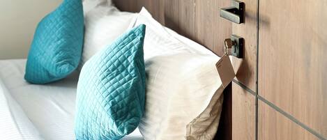 A bed with white linens and teal pillows, a wooden headboard, and a door with a handle and lock.
