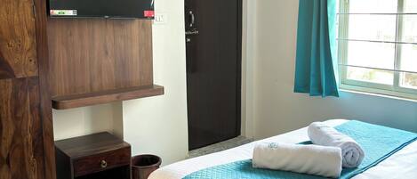 Un dormitorio con una cama, un armario de madera, un televisor montado en la pared y una ventana con cortinas.