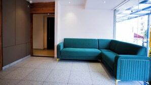 Un soggiorno moderno con un divano a divano color petrolio, una ventola a soffitto e un'ampia finestra con vista sulla città.