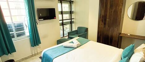 A hotel room with a bed, a chair, a TV, a wardrobe, and a window with curtains.