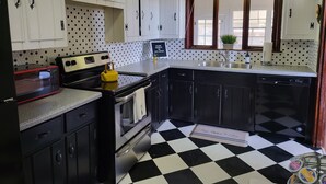 Une cuisine avec un carrelage noir et blanc, des meubles blancs dotés de poignées noires, une bouilloire jaune, un four à micro-ondes, une cuisinière et un évier.