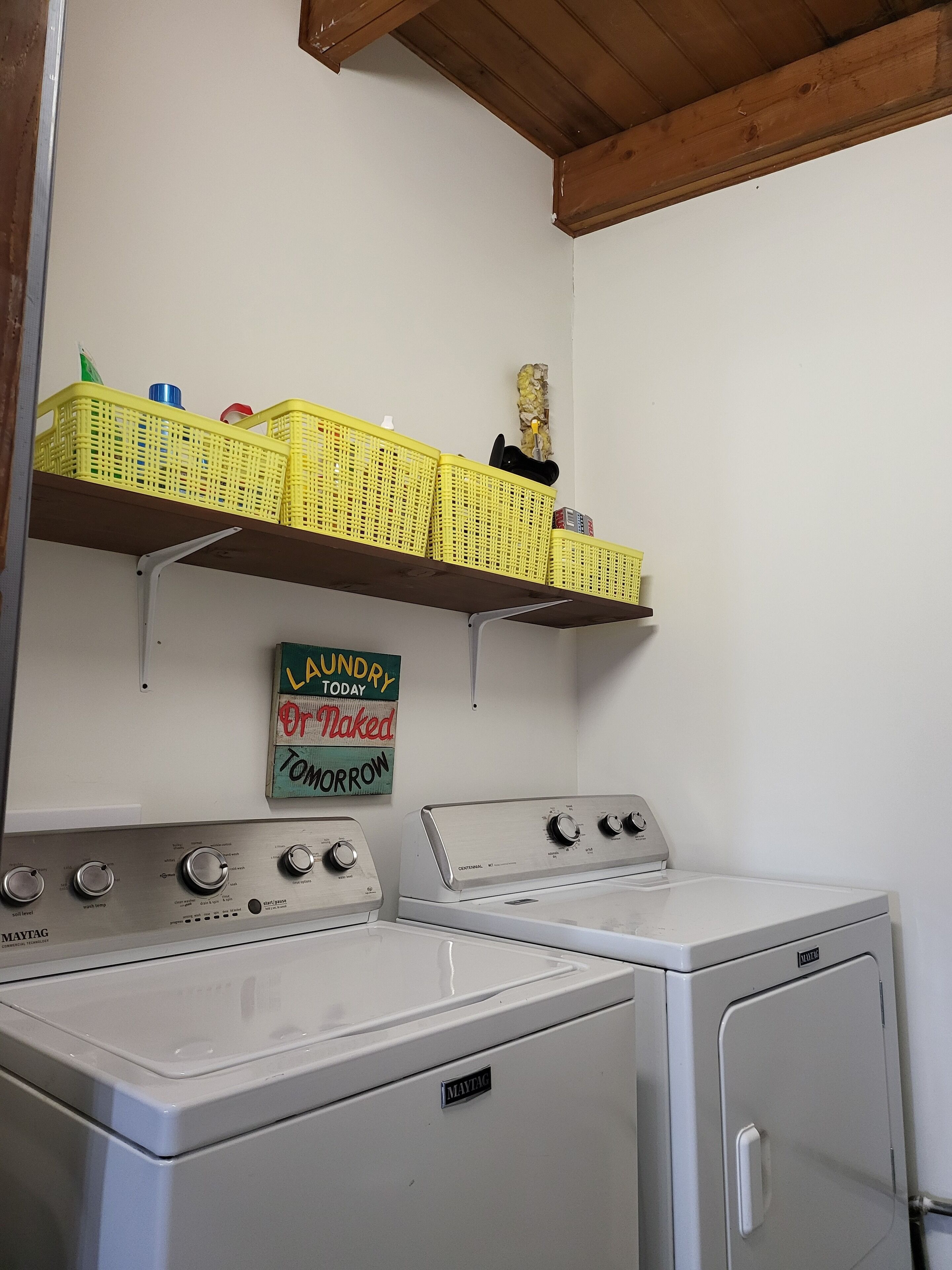 Un espace buanderie équipé de deux machines à laver et deux sèche-linge Maytag, d’une étagère avec des paniers et d’un panneau indiquant qu’il s’agit de la buanderie.