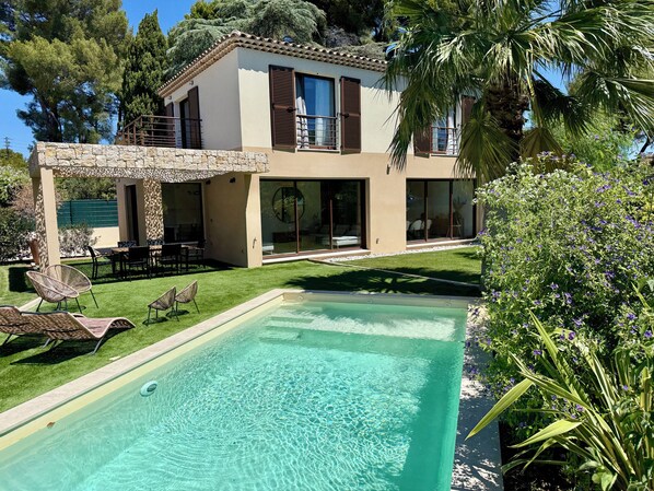A modern house with a swimming pool, outdoor seating, and a stone wall.