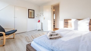 A bedroom with a bed, a chair, a nightstand, a mirror, and a door leading to another room.