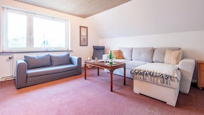 A living room with a grey sofa, a beige sofa, a wooden coffee table, and a window with blinds.