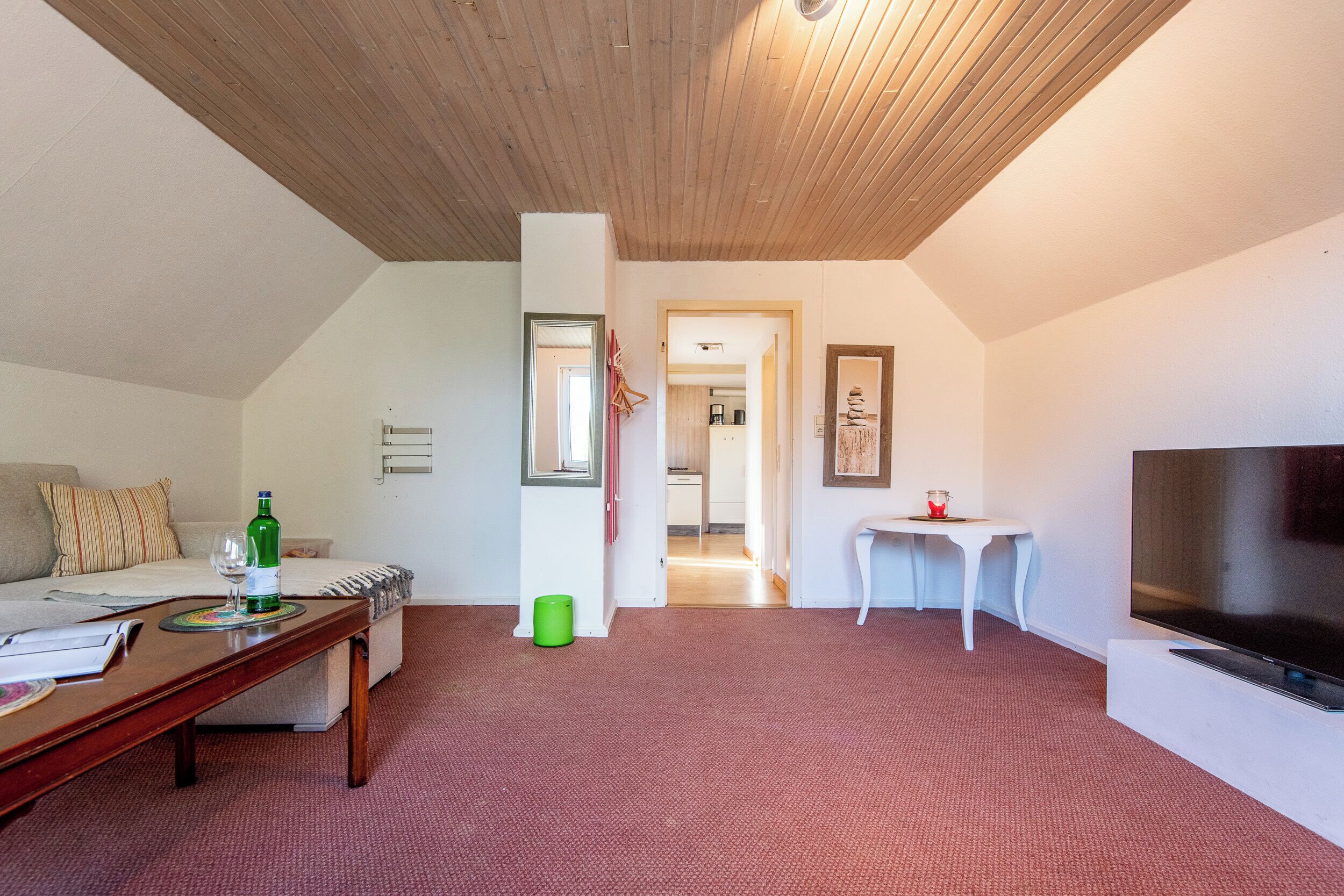 Una sala de estar acogedora con techo de madera, un televisor, un sofá, una mesa de centro y una mesita con una vela roja.