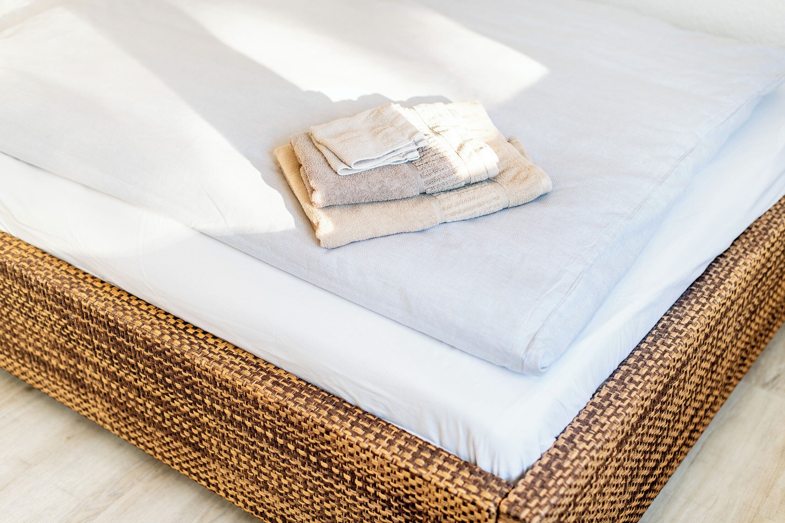 A neatly made bed with white linens and a folded towel on top.